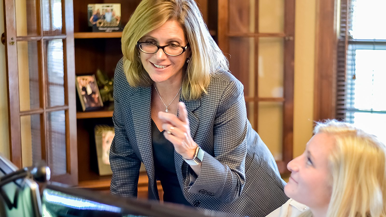 Sarah pointing over woman's shoulder by computer screen