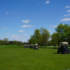 Golf carts with golfers and equiptment drive on the green grass